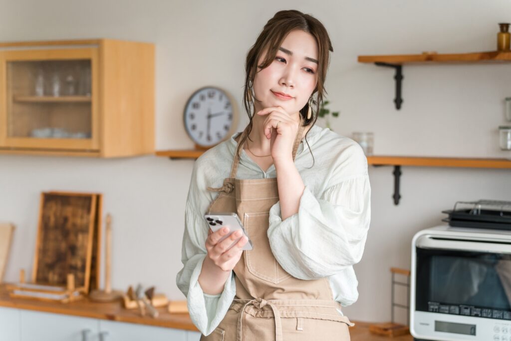 キッチンでサプリメントを手に持ち、栄養バランスについて考える女性のイメージ画像
