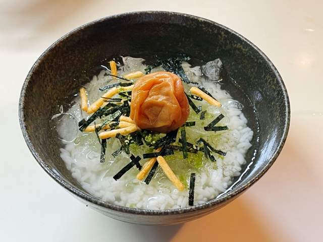 黒い器に盛られた冷やし茶漬け。中央に梅干しを置き、刻み海苔や細切りの具材を散らした写真
