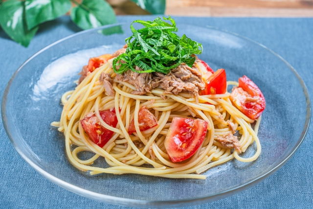 青い皿に盛られた冷製パスタ。ツナ、カットトマト、細切りの青じそをトッピングした料理写真